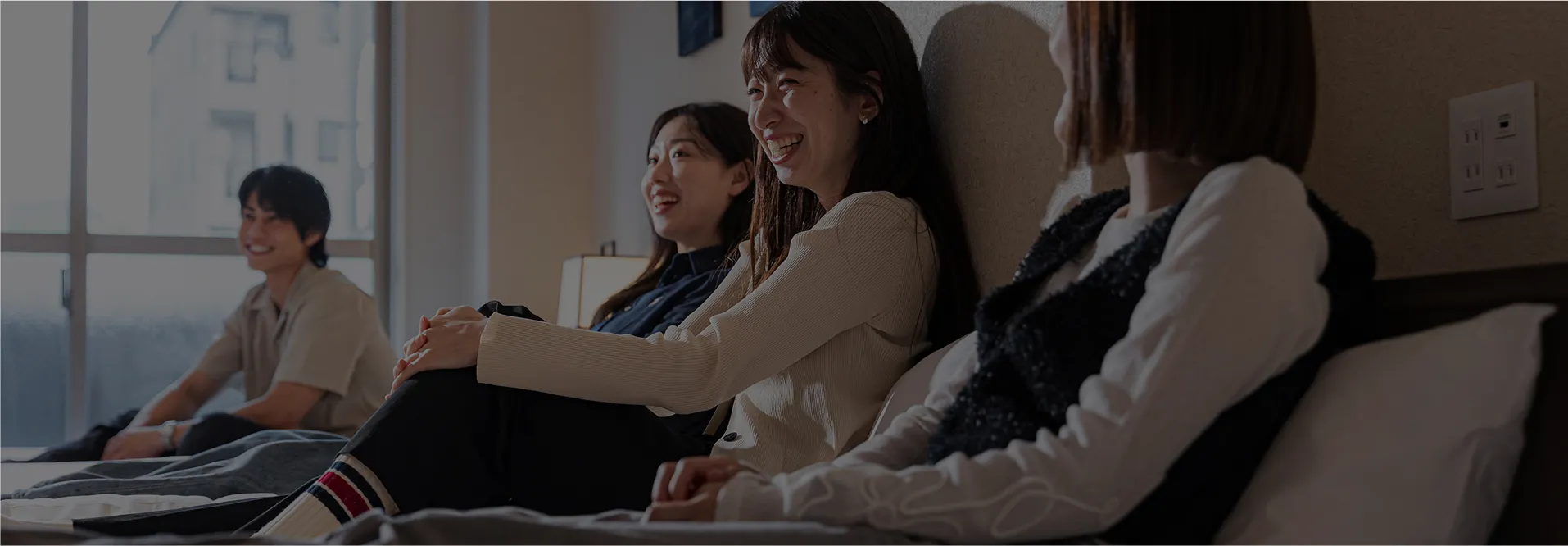 ホテルの客室。ベッドの上に座る若い女性が笑顔でくつろぐ様子。