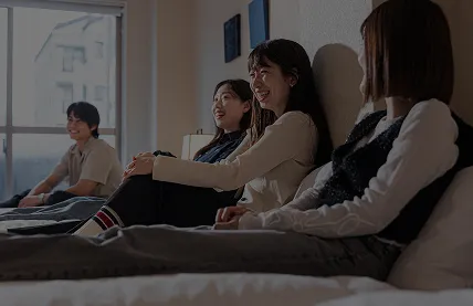 ホテルの客室。ベッドの上に座る若い女性が笑顔でくつろぐ様子。